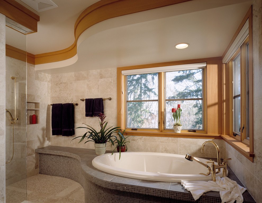 Cette image montre une grande salle de bain principale design avec un carrelage beige, une baignoire posée, des carreaux de céramique, un mur beige, un sol en travertin, un sol beige et une fenêtre.