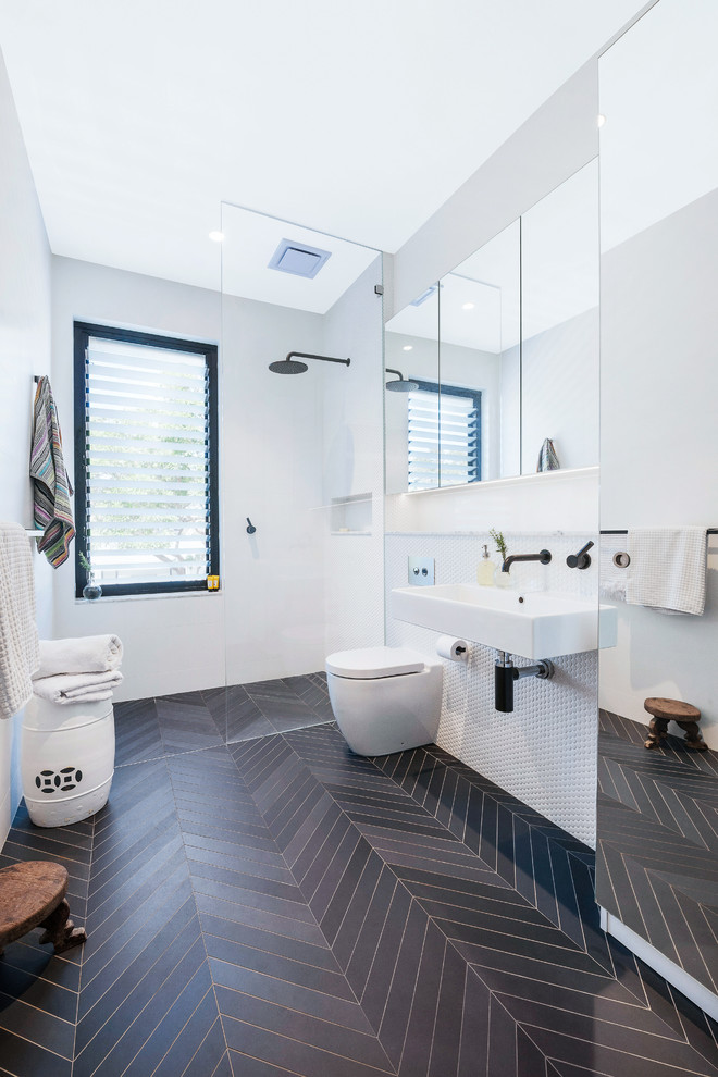 Modern inredning av ett vit vitt badrum med dusch, med en kantlös dusch, en toalettstol med hel cisternkåpa, vit kakel, vita väggar, ett väggmonterat handfat, grått golv och med dusch som är öppen
