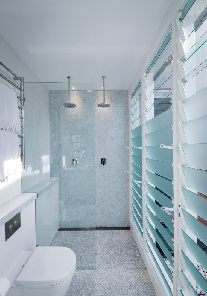 Exemple d'une salle de bain principale tendance de taille moyenne avec un placard à porte plane, des portes de placard blanches, une douche double, WC suspendus, un carrelage blanc, un carrelage de pierre, un mur blanc, un sol en galet, une vasque et un plan de toilette en marbre.
