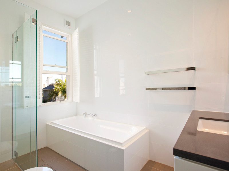 Kleines Modernes Badezimmer mit Eckbadewanne, Eckdusche, weißen Fliesen, Porzellanfliesen, weißer Wandfarbe, Keramikboden, integriertem Waschbecken, Granit-Waschbecken/Waschtisch, braunem Boden und Falttür-Duschabtrennung in Sydney