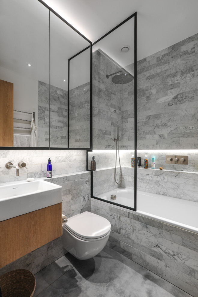 Idéer för att renovera ett mellanstort funkis vit vitt badrum med dusch, med släta luckor, beige skåp, ett badkar i en alkov, en dusch/badkar-kombination, en vägghängd toalettstol, grå kakel, ett integrerad handfat och grått golv