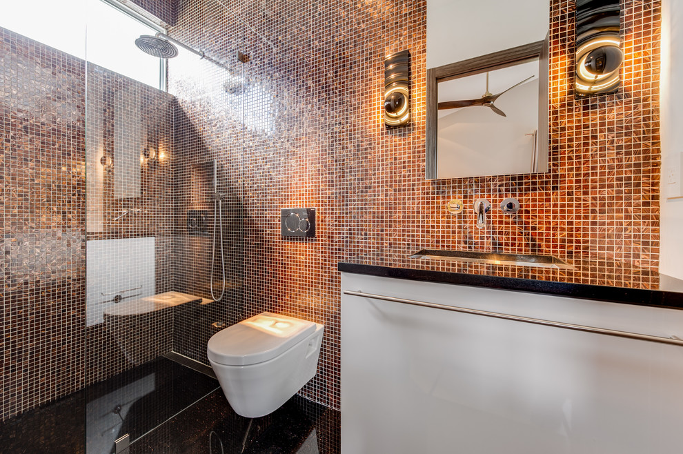 Bild på ett funkis badrum med dusch, med en kantlös dusch, en vägghängd toalettstol, orange kakel, flerfärgad kakel, bänkskiva i akrylsten, släta luckor, vita skåp, mosaik, ett undermonterad handfat och med dusch som är öppen