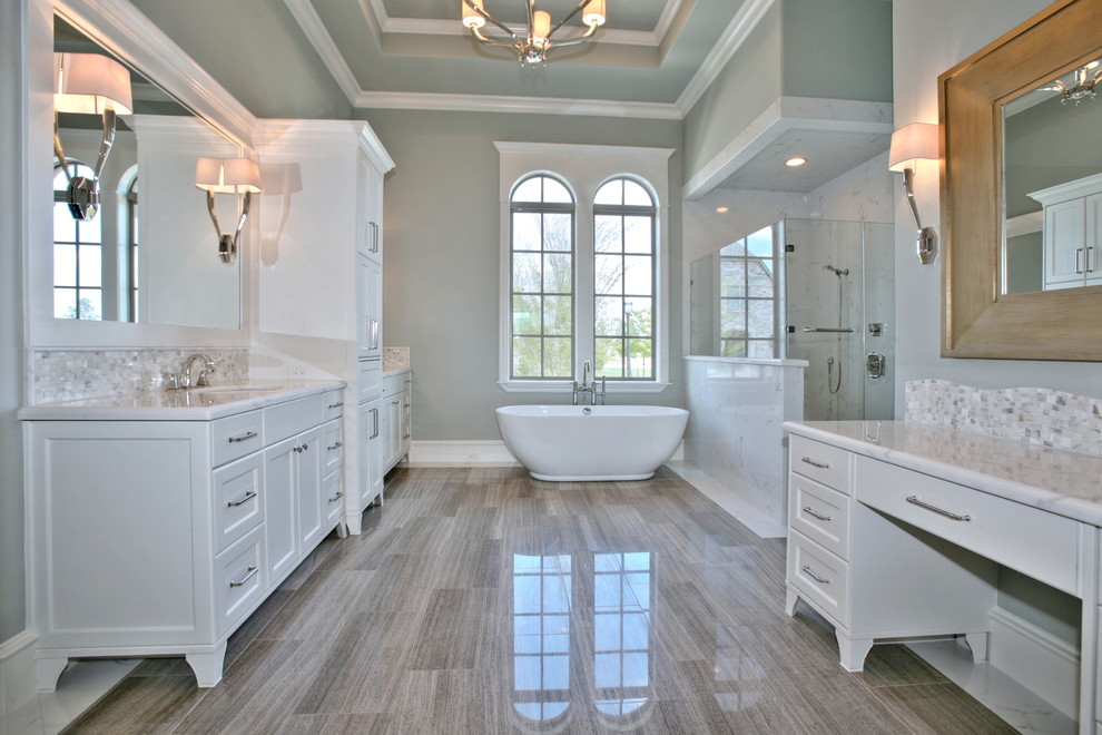Cette photo montre une salle de bain principale tendance avec un lavabo encastré, un placard avec porte à panneau encastré, des portes de placard blanches, un plan de toilette en marbre, une baignoire indépendante, une douche d'angle et un mur gris.