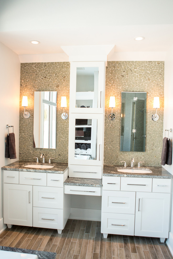 Exemple d'une douche en alcôve chic avec un placard à porte shaker, des portes de placard blanches, une baignoire indépendante, WC à poser, un carrelage de pierre, un mur blanc, un sol en bois brun, un lavabo encastré et un plan de toilette en granite.