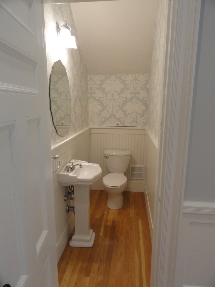 Diseño de cuarto de baño clásico pequeño con lavabo con pedestal, sanitario de una pieza, paredes azules, suelo de madera clara y aseo y ducha