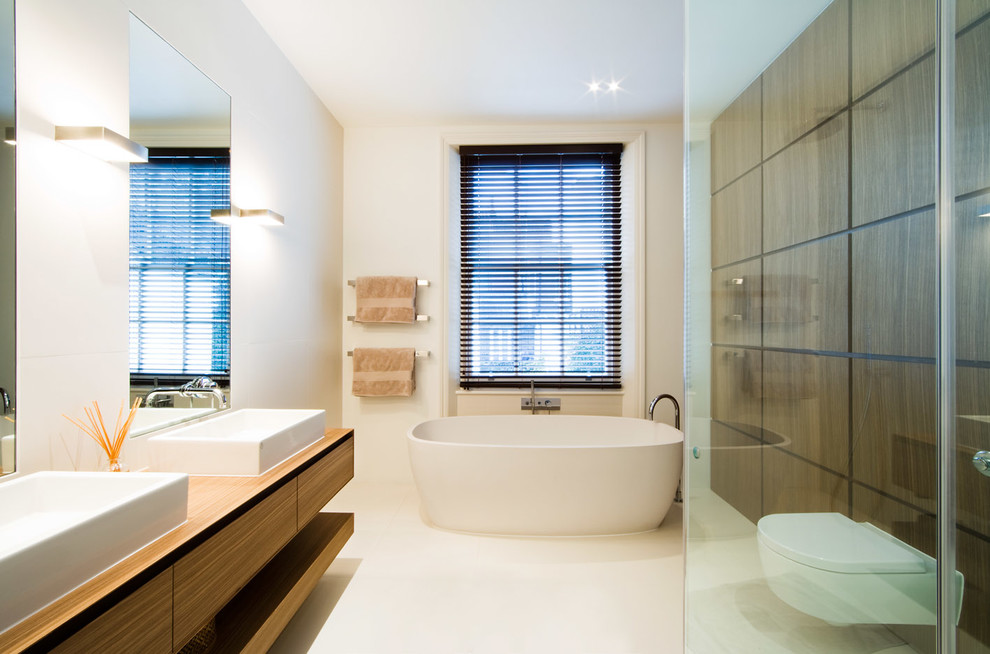 Example of a large trendy white tile and stone tile bathroom design in London with a vessel sink, flat-panel cabinets, medium tone wood cabinets, wood countertops, a wall-mount toilet, white walls and brown countertops