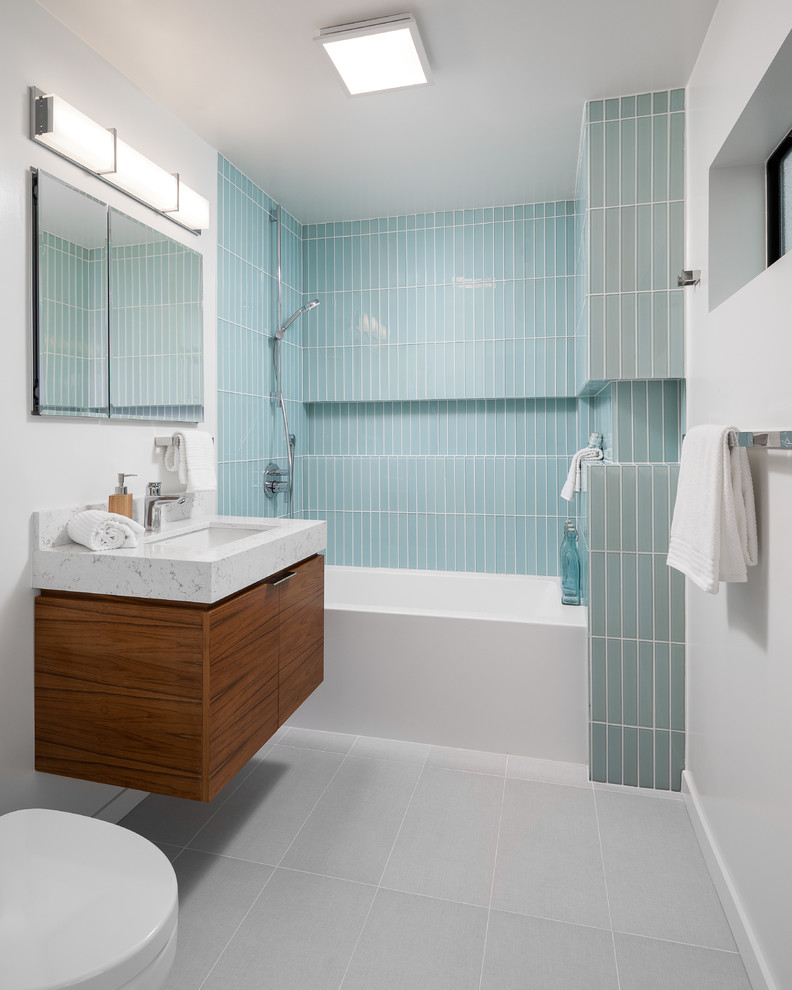 Modelo de cuarto de baño contemporáneo con armarios con paneles lisos, puertas de armario de madera oscura, sanitario de pared, baldosas y/o azulejos azules, paredes blancas, suelo de pizarra, lavabo suspendido, encimera de mármol, suelo gris, ducha con cortina y encimeras blancas