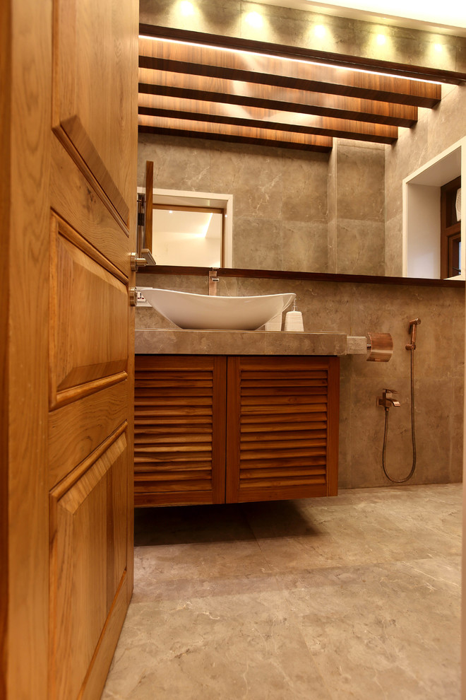 Mittelgroßes Modernes Duschbad mit Lamellenschränken, hellbraunen Holzschränken, Wandtoilette mit Spülkasten, grauen Fliesen, Steinfliesen, grauer Wandfarbe, Keramikboden und gefliestem Waschtisch in Pune