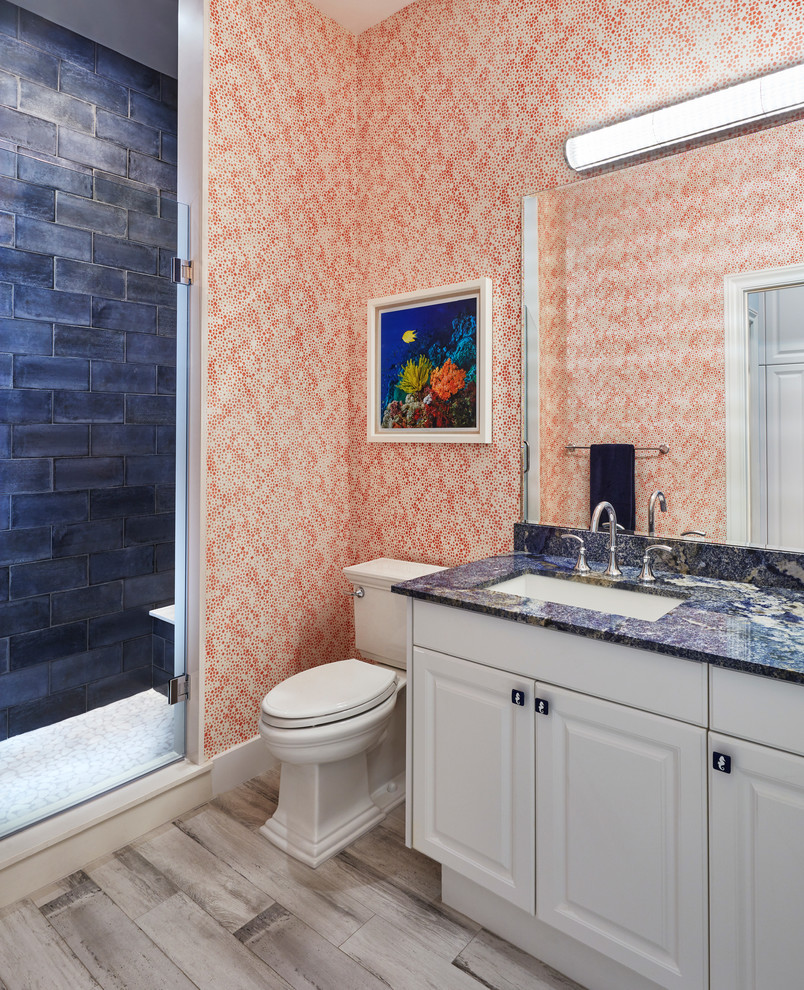 Bild på ett maritimt blå blått badrum med dusch, med luckor med upphöjd panel, vita skåp, en toalettstol med separat cisternkåpa, blå kakel, orange väggar, ett undermonterad handfat och beiget golv