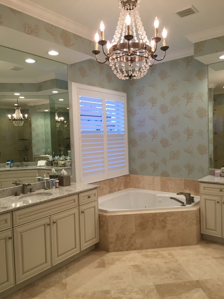 Photo of a nautical ensuite bathroom in Miami with raised-panel cabinets, white cabinets, a corner bath, beige tiles, stone tiles, light hardwood flooring, a submerged sink and engineered stone worktops.