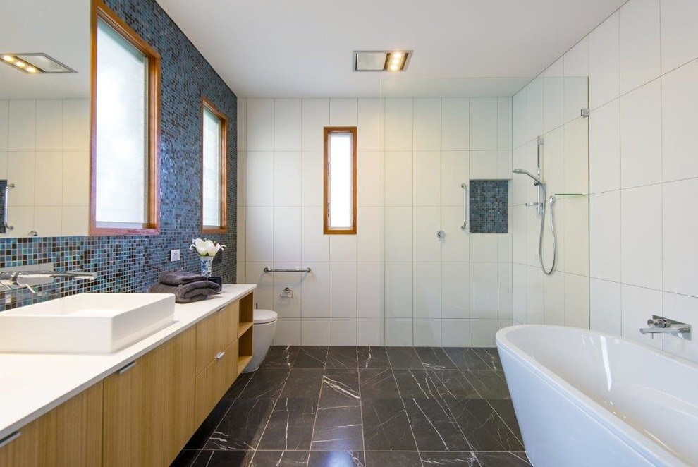 Aménagement d'une salle de bain contemporaine en bois clair avec un placard à porte plane, une baignoire indépendante, une douche ouverte, un carrelage bleu, mosaïque, une vasque et un sol gris.