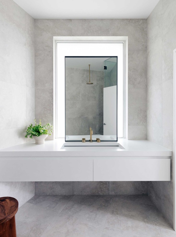 Aménagement d'une salle de bain bord de mer avec un placard à porte plane, des portes de placard blanches, un carrelage gris, un mur gris, un lavabo encastré, un sol gris et un plan de toilette blanc.