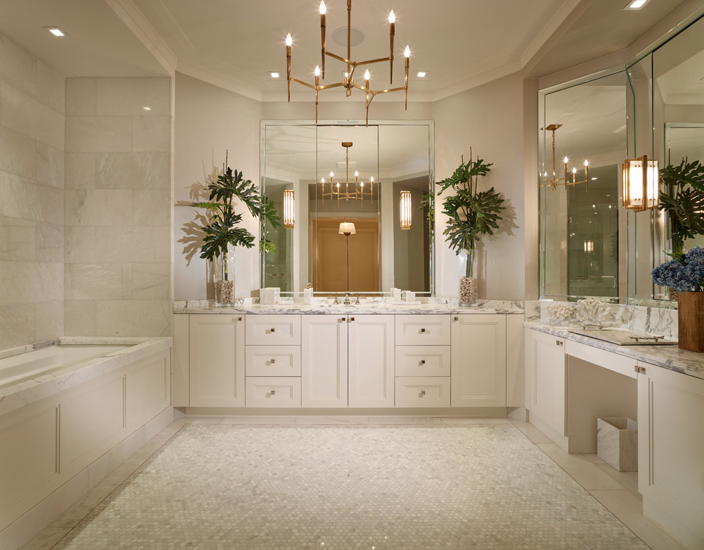 На фото: большая главная ванная комната в стиле неоклассика (современная классика) с фасадами с утопленной филенкой, белыми фасадами, полновстраиваемой ванной, белой плиткой, каменной плиткой, белыми стенами, мраморным полом, врезной раковиной и мраморной столешницей с