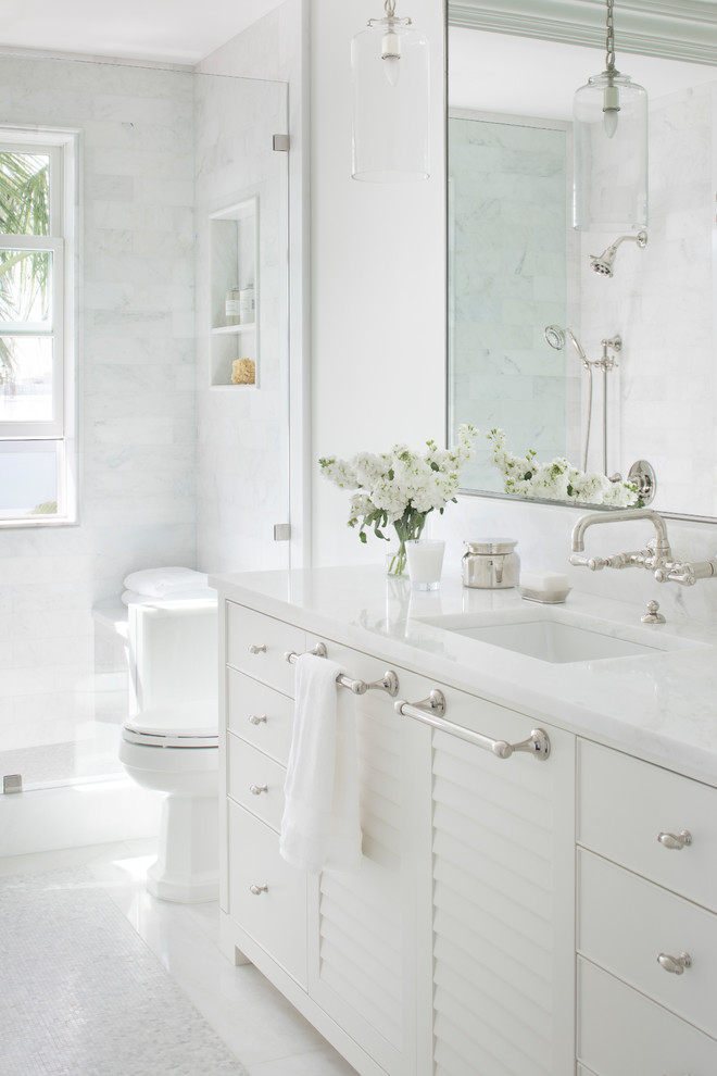 На фото: ванная комната в морском стиле с фасадами с филенкой типа жалюзи, белыми фасадами, белой плиткой, белыми стенами, врезной раковиной, белым полом, белой столешницей и окном с