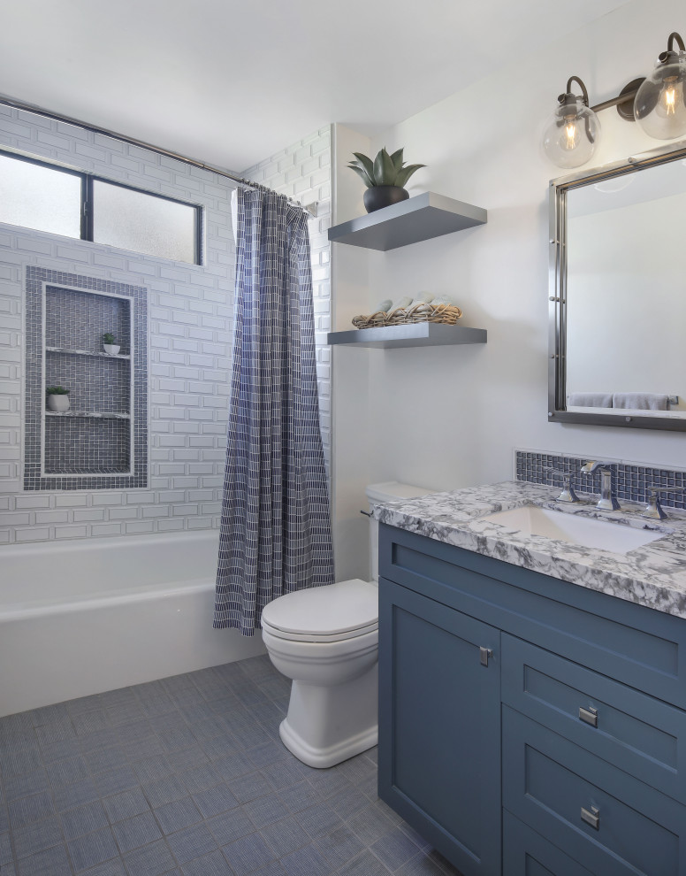 This is an example of a classic family bathroom in Orange County with shaker cabinets, blue cabinets, an alcove bath, a shower/bath combination, a two-piece toilet, white tiles, ceramic tiles, white walls, marble flooring, a submerged sink, engineered stone worktops, blue floors, a shower curtain, grey worktops, a wall niche, a single sink and a built in vanity unit.