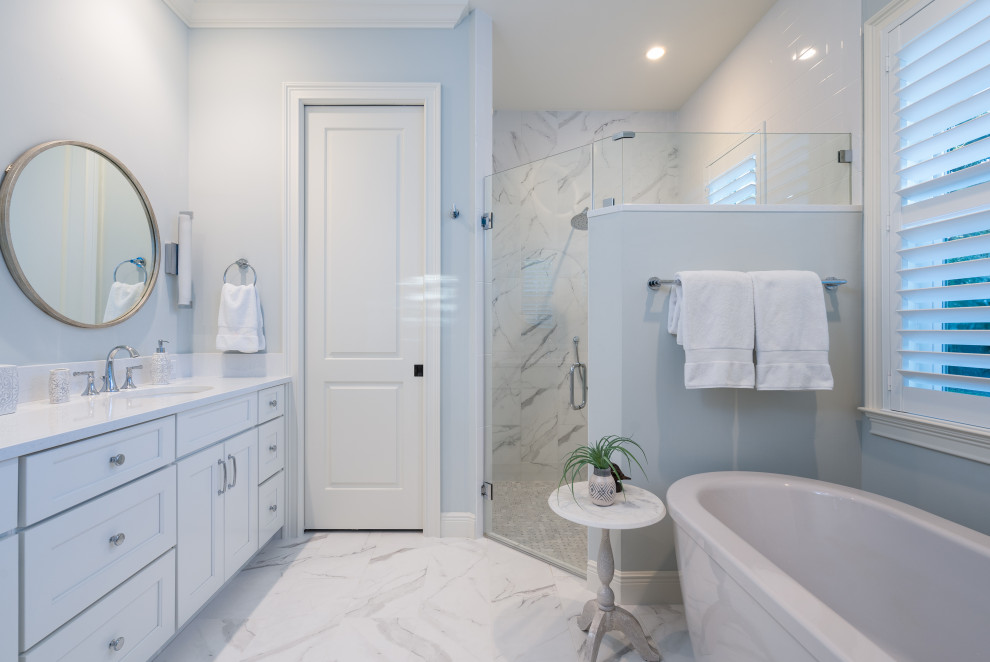На фото: большая главная ванная комната в морском стиле с фасадами в стиле шейкер, белыми фасадами, отдельно стоящей ванной, угловым душем, белой плиткой, мраморной плиткой, синими стенами, врезной раковиной, столешницей из искусственного кварца, душем с распашными дверями, белой столешницей, мраморным полом и белым полом