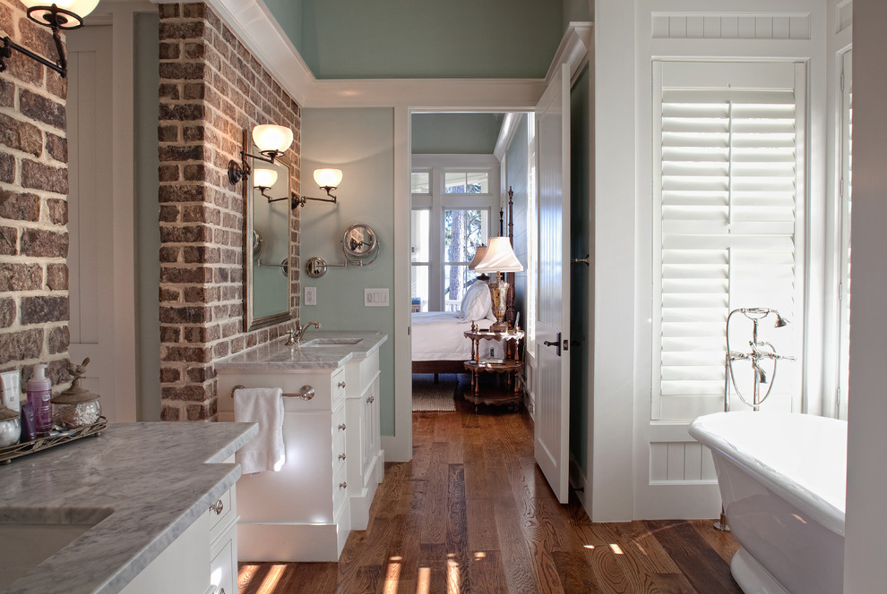 Idée de décoration pour une grande salle de bain principale marine avec un lavabo encastré, des portes de placard blanches, un plan de toilette en marbre, une baignoire indépendante, un mur vert et un sol en bois brun.