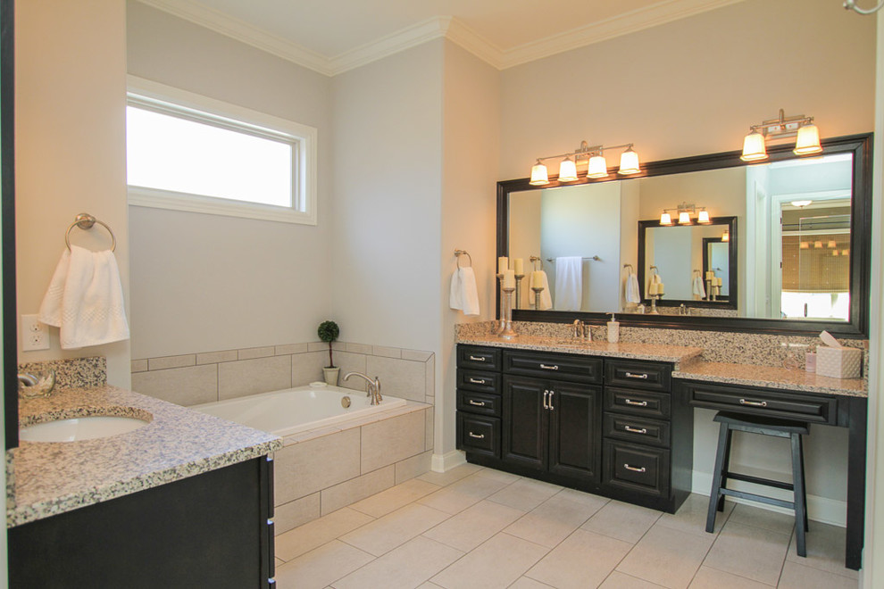 Photo of a large traditional ensuite bathroom in Nashville with raised-panel cabinets, black cabinets, a built-in bath, an alcove shower, a two-piece toilet, beige tiles, brown tiles, grey tiles, ceramic tiles, grey walls, porcelain flooring, a submerged sink, granite worktops, beige floors and a hinged door.