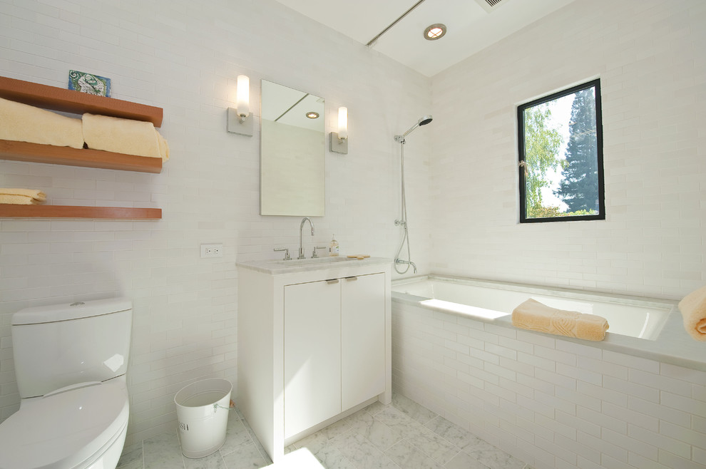 Пример оригинального дизайна: ванная комната в стиле модернизм с врезной раковиной, плоскими фасадами, белыми фасадами, полновстраиваемой ванной, душем над ванной, раздельным унитазом, белой плиткой и плиткой кабанчик