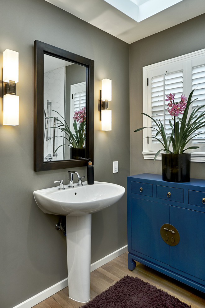 Small traditional shower room bathroom in San Francisco with flat-panel cabinets, blue cabinets, a corner bath, a shower/bath combination, a one-piece toilet, white tiles, ceramic tiles, grey walls, light hardwood flooring, a pedestal sink, yellow floors, an open shower and white worktops.