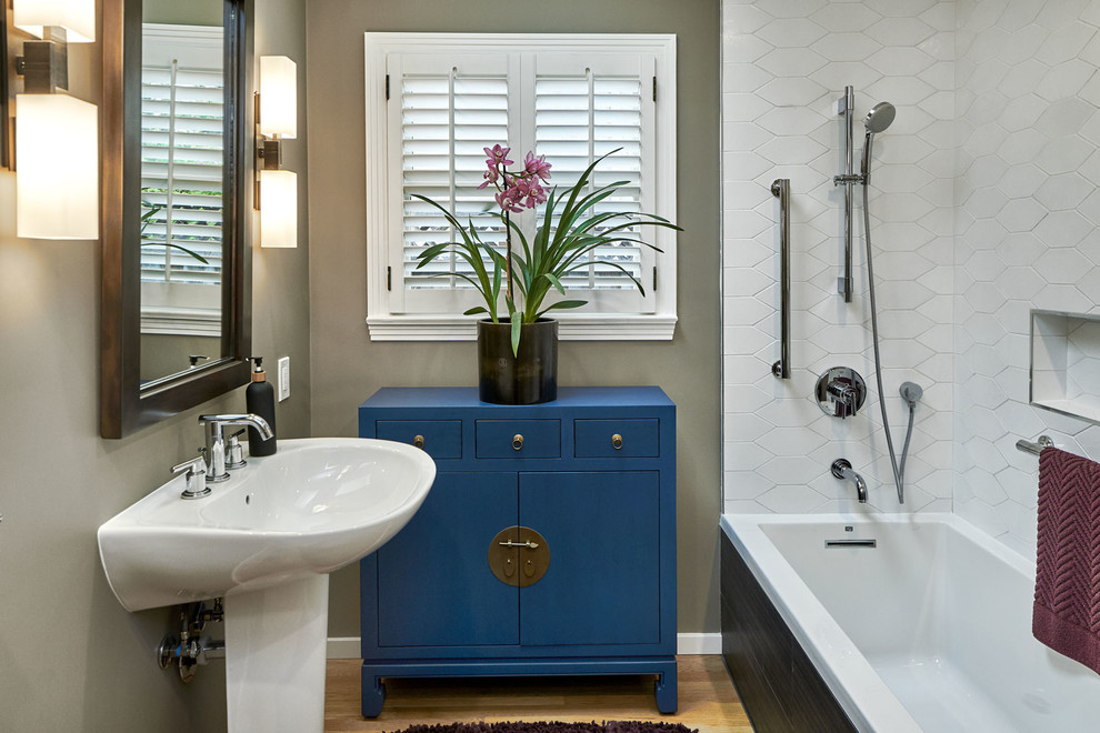 Klassisk inredning av ett litet vit vitt badrum med dusch, med släta luckor, blå skåp, ett hörnbadkar, en dusch/badkar-kombination, en toalettstol med hel cisternkåpa, vit kakel, keramikplattor, grå väggar, ljust trägolv, ett piedestal handfat, gult golv och med dusch som är öppen