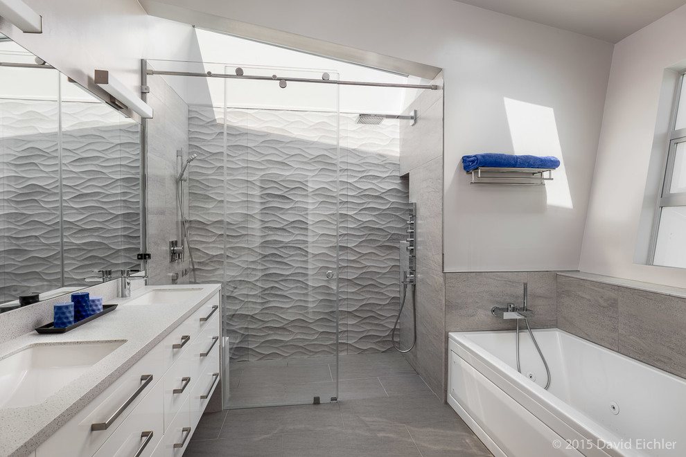 Modern inredning av ett en-suite badrum, med ett undermonterad handfat, släta luckor, vita skåp, bänkskiva i akrylsten, ett badkar i en alkov, en kantlös dusch, grå kakel och keramikplattor