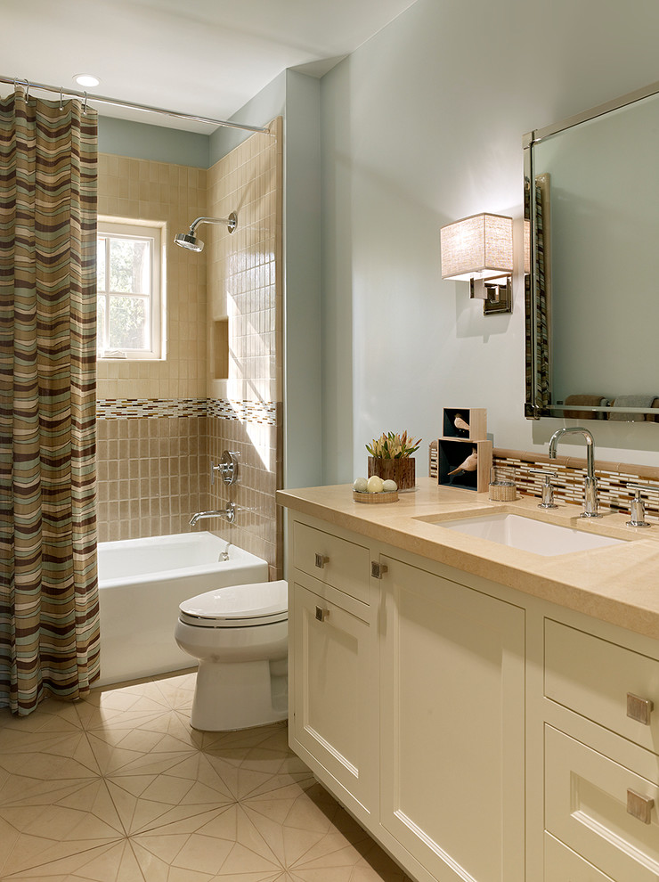 Klassisk inredning av ett mellanstort badrum, med ett undermonterad handfat, luckor med infälld panel, vita skåp, ett platsbyggt badkar, en dusch/badkar-kombination, en toalettstol med hel cisternkåpa, beige kakel, stenkakel, blå väggar, mosaikgolv och dusch med duschdraperi