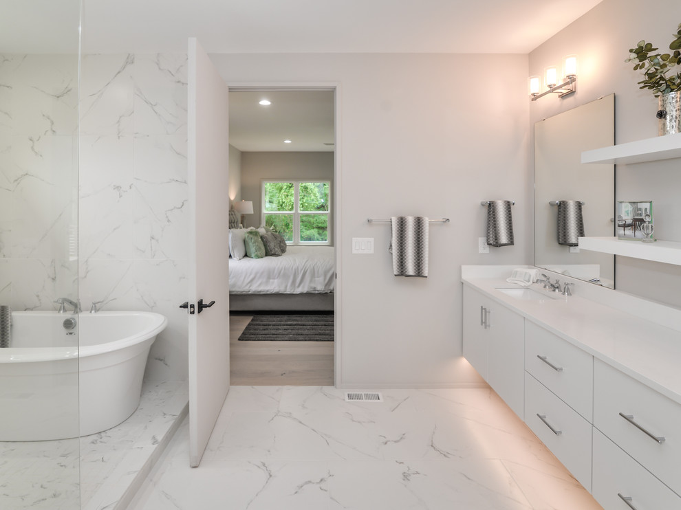 Example of a large minimalist master white tile and marble tile marble floor and white floor bathroom design in Charlotte with flat-panel cabinets, white cabinets, a one-piece toilet, gray walls, an undermount sink, quartz countertops and white countertops