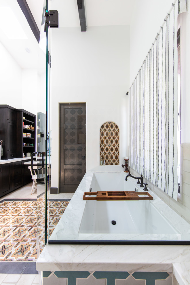 Mediterranean ensuite bathroom in Los Angeles with recessed-panel cabinets, dark wood cabinets, a submerged bath, beige tiles, white walls, multi-coloured floors and white worktops.