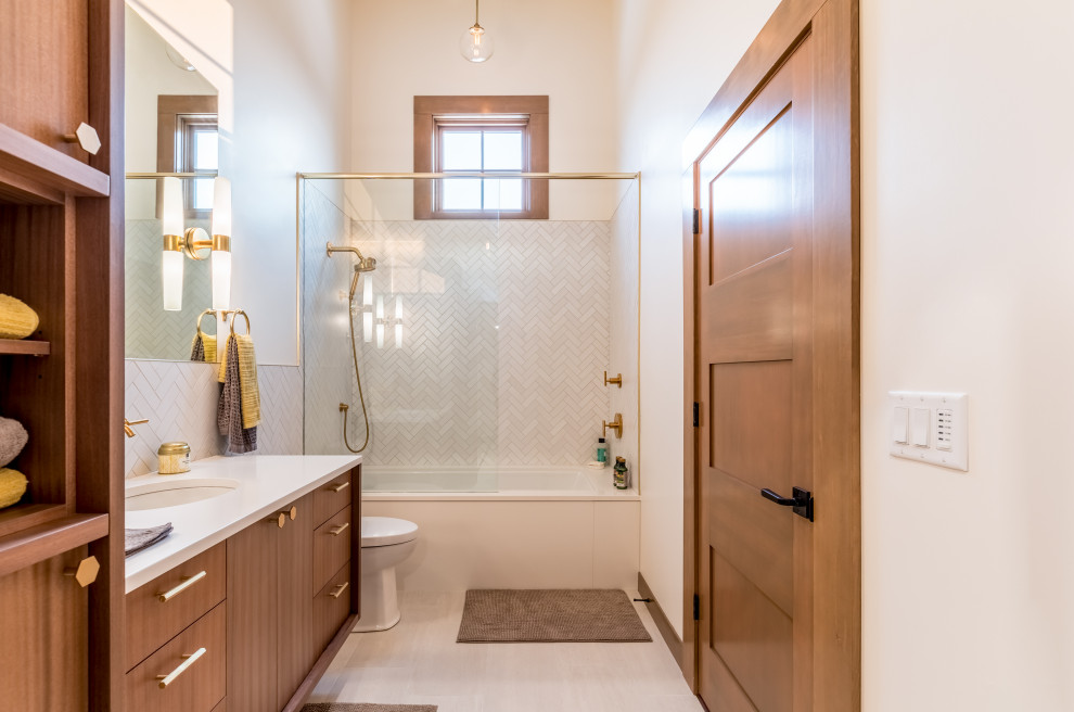 シアトルにあるトランジショナルスタイルのおしゃれな浴室 (フラットパネル扉のキャビネット、中間色木目調キャビネット、アルコーブ型浴槽、シャワー付き浴槽	、白いタイル、白い壁、アンダーカウンター洗面器、白い床、白い洗面カウンター) の写真