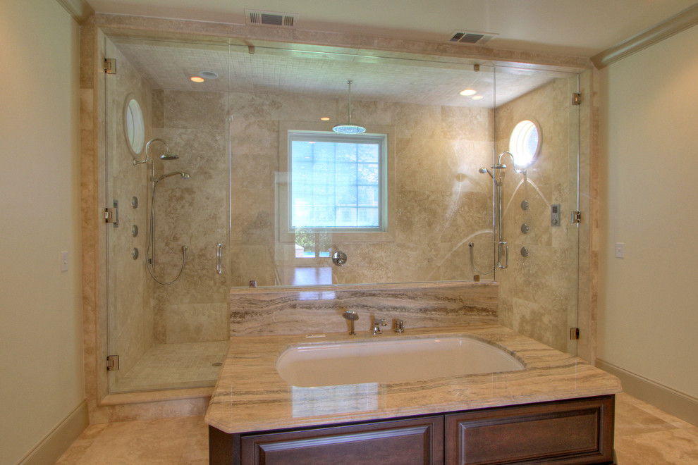 Cette photo montre une très grande salle de bain principale en bois foncé avec un lavabo encastré, un placard avec porte à panneau surélevé, une baignoire encastrée, une douche double, un carrelage beige, un carrelage de pierre, un mur beige et un sol en travertin.