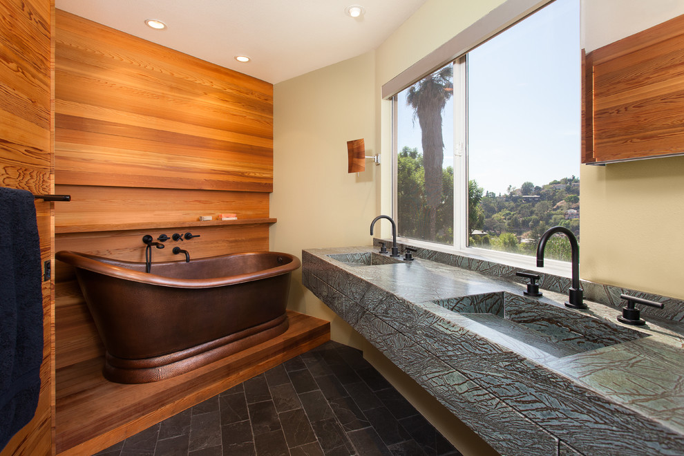 Bild på ett mellanstort funkis en-suite badrum, med släta luckor, gröna skåp, ett fristående badkar, en toalettstol med separat cisternkåpa, skiffergolv, ett integrerad handfat, marmorbänkskiva, svart golv och orange väggar