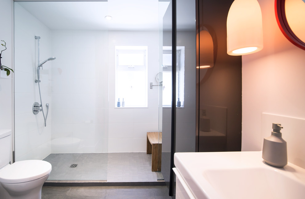 Inredning av ett modernt badrum, med vita skåp, en dusch i en alkov, en toalettstol med separat cisternkåpa, vit kakel, grått golv och med dusch som är öppen