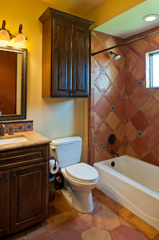 Aménagement d'une salle de bain sud-ouest américain en bois foncé avec un lavabo encastré, un placard avec porte à panneau surélevé, une baignoire en alcôve, un combiné douche/baignoire, des carreaux en terre cuite, tomettes au sol et un carrelage marron.