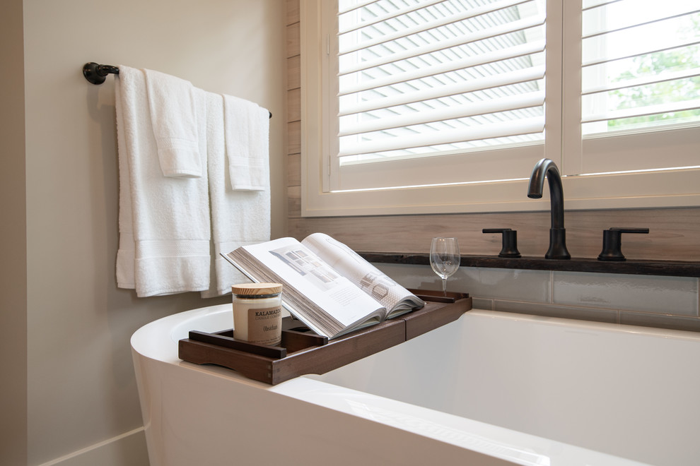 This is an example of a medium sized classic ensuite bathroom in Grand Rapids with raised-panel cabinets, brown cabinets, a freestanding bath, an alcove shower, a two-piece toilet, grey tiles, porcelain tiles, grey walls, porcelain flooring, a submerged sink, marble worktops, white floors, a hinged door and white worktops.