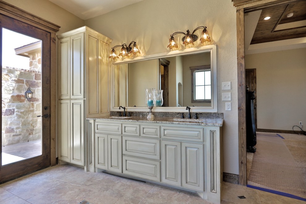 Mid-sized tuscan master beige tile and stone tile porcelain tile bathroom photo in Dallas with an undermount sink, shaker cabinets, distressed cabinets, granite countertops, a two-piece toilet and beige walls