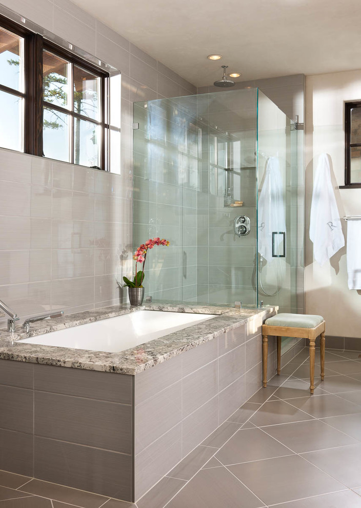 Modelo de cuarto de baño principal rural grande con lavabo sobreencimera, puertas de armario de madera en tonos medios, encimera de granito, bañera encastrada sin remate y baldosas y/o azulejos grises