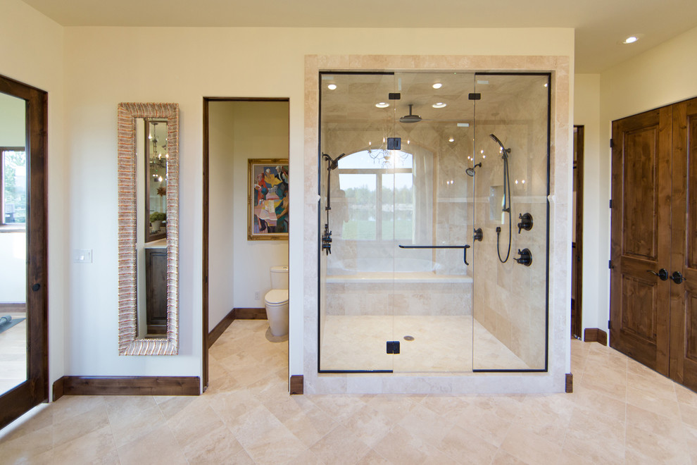 Example of a large classic master limestone floor and beige floor bathroom design in Boise with raised-panel cabinets, medium tone wood cabinets, a one-piece toilet, beige walls, an undermount sink, limestone countertops and a hinged shower door
