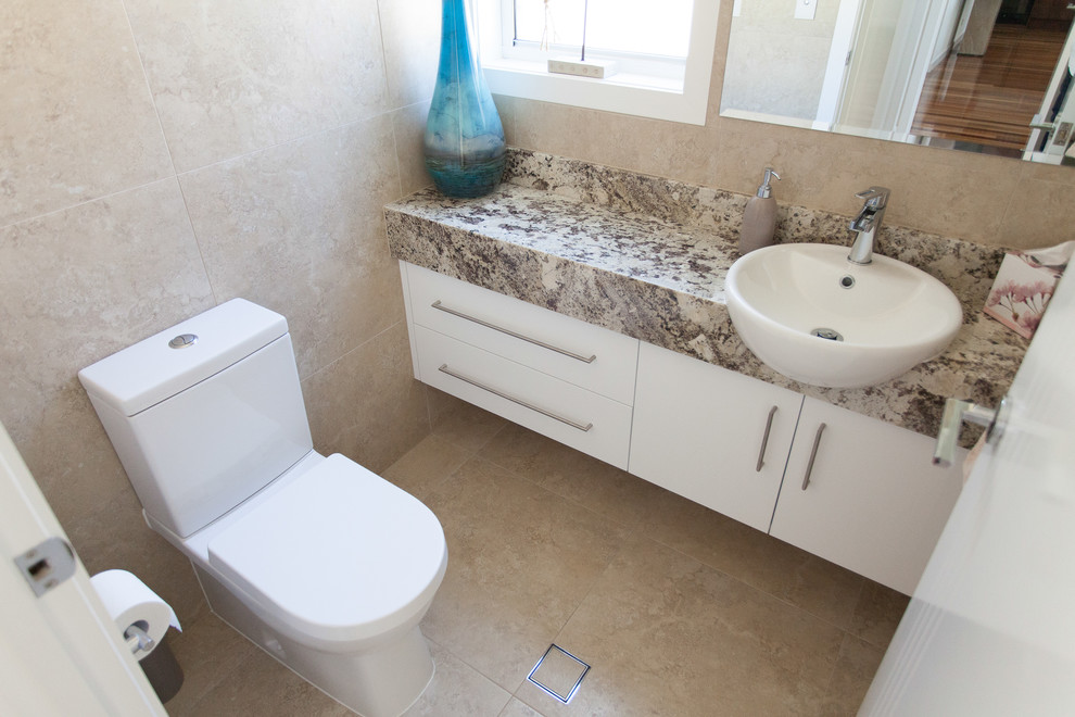 Diseño de cuarto de baño actual con armarios con paneles lisos, puertas de armario blancas, sanitario de una pieza, baldosas y/o azulejos beige, paredes beige y lavabo encastrado