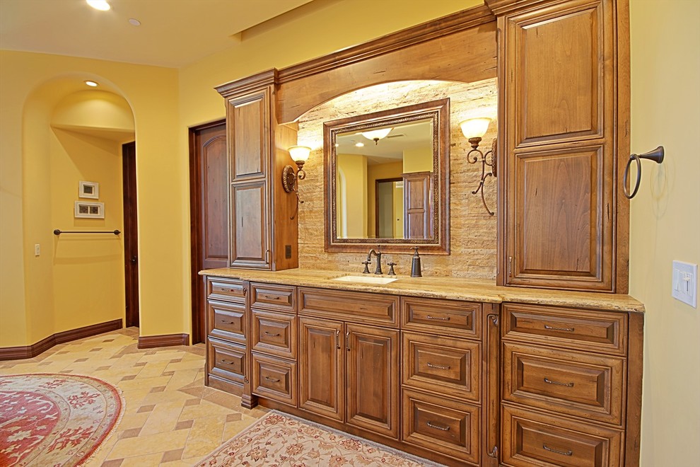 Foto på ett stort medelhavsstil en-suite badrum, med luckor med upphöjd panel, skåp i mellenmörkt trä, ett fristående badkar, beige kakel, stenkakel, gula väggar, ett undermonterad handfat, granitbänkskiva och travertin golv