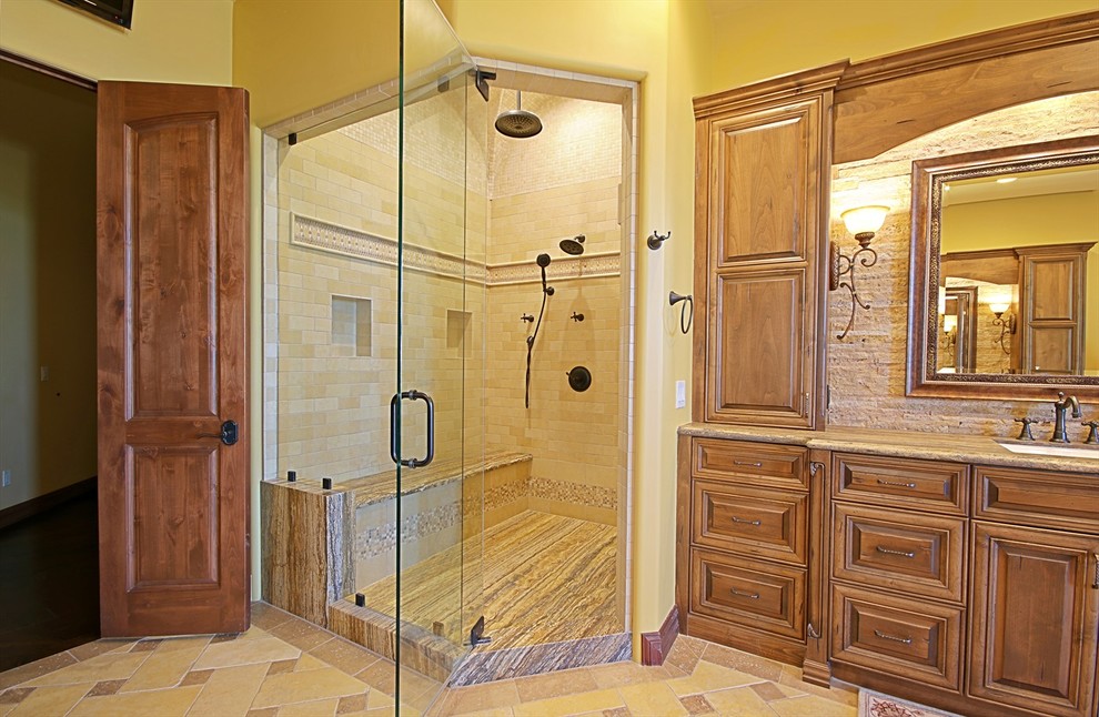 Cette photo montre une grande salle de bain principale méditerranéenne en bois brun avec un placard avec porte à panneau surélevé, une baignoire indépendante, un carrelage beige, un carrelage de pierre, un mur jaune, un lavabo encastré, un plan de toilette en granite, un espace douche bain et un sol en travertin.