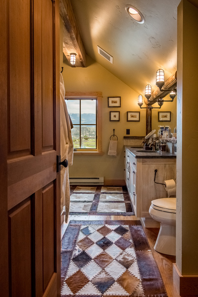 Example of a mid-sized mountain style 3/4 medium tone wood floor and brown floor bathroom design in Other with shaker cabinets, distressed cabinets, a two-piece toilet, beige walls, an undermount sink and quartzite countertops
