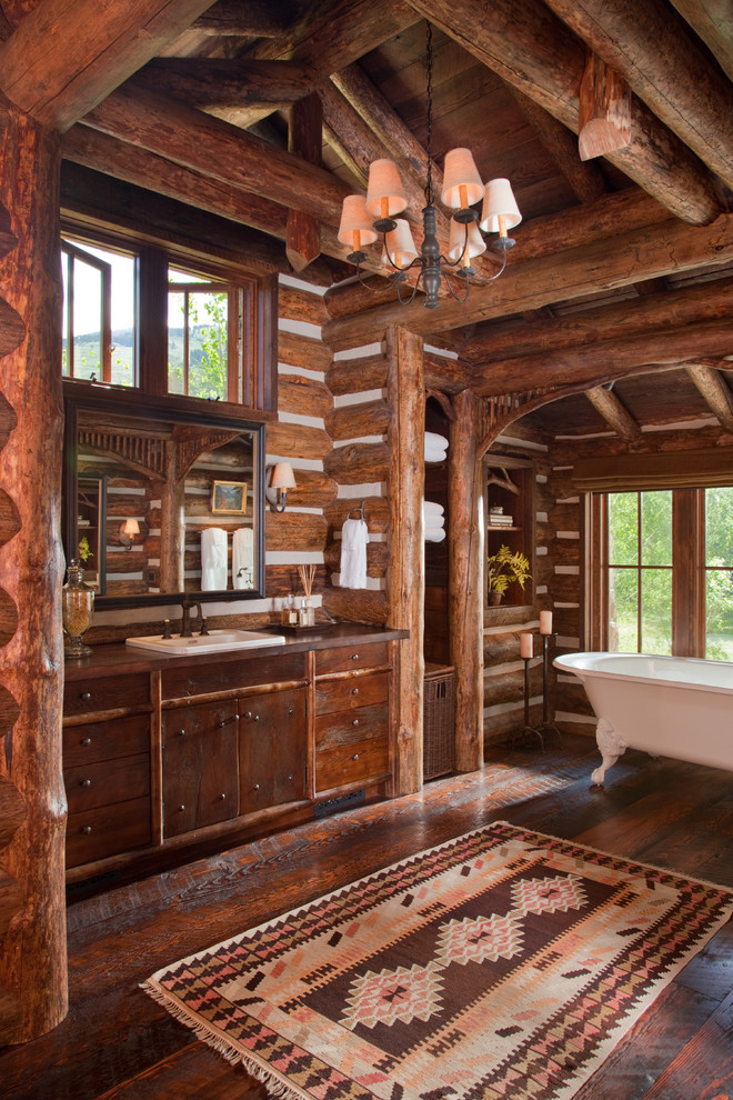 Пример оригинального дизайна: большая главная ванная комната в деревянном доме в стиле рустика с темными деревянными фасадами, ванной на ножках, коричневыми стенами, темным паркетным полом, накладной раковиной, столешницей из дерева, коричневым полом и плоскими фасадами