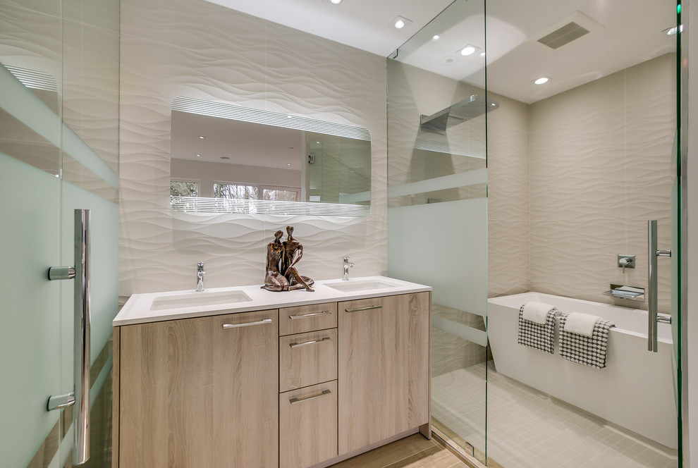 Foto på ett mellanstort funkis badrum, med släta luckor, skåp i ljust trä, ett fristående badkar, vit kakel, porslinskakel, beige väggar, ett undermonterad handfat, bänkskiva i akrylsten och med dusch som är öppen