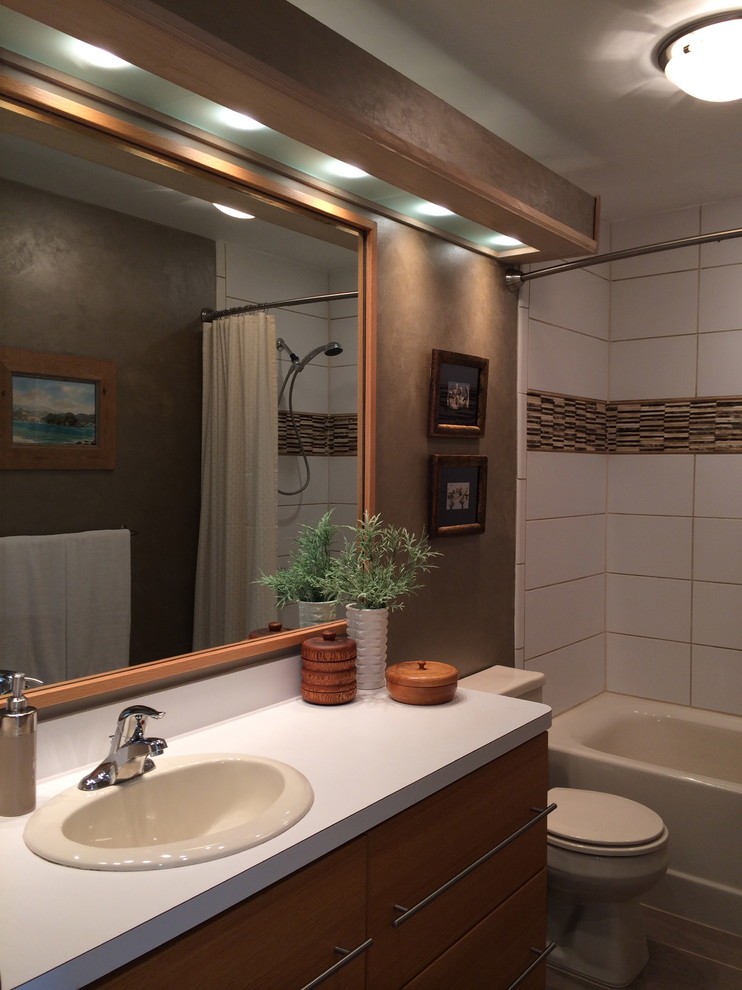Klassisk inredning av ett litet en-suite badrum, med ett nedsänkt handfat, släta luckor, skåp i ljust trä, laminatbänkskiva, ett badkar i en alkov, en dusch/badkar-kombination, en toalettstol med hel cisternkåpa, flerfärgad kakel, stenkakel, bruna väggar och klinkergolv i porslin