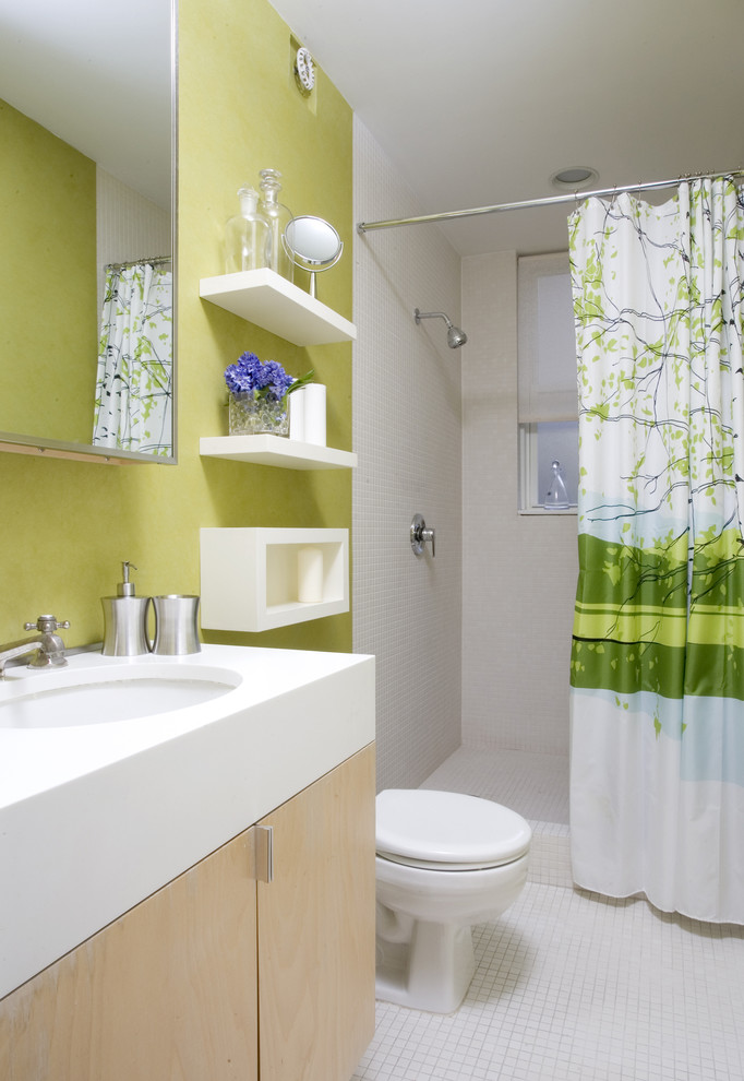 Modelo de cuarto de baño actual con armarios con paneles lisos, puertas de armario de madera clara, ducha empotrada, paredes verdes, suelo con mosaicos de baldosas y ducha con cortina