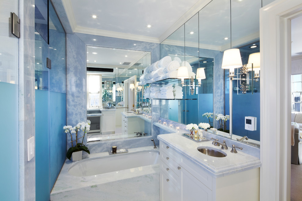 Cette image montre une salle de bain design avec un lavabo encastré, un placard avec porte à panneau encastré, des portes de placard blanches, un plan de toilette en marbre et une baignoire en alcôve.