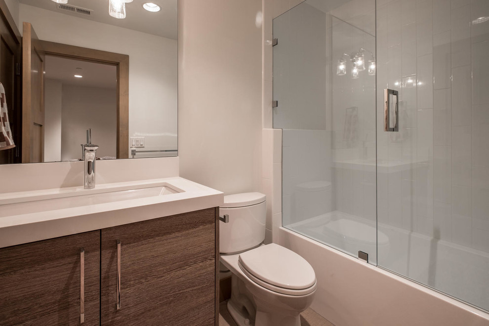 This is an example of a small contemporary shower room bathroom in Salt Lake City with flat-panel cabinets, medium wood cabinets, an alcove bath, a shower/bath combination, a one-piece toilet, white tiles, ceramic tiles, white walls, a submerged sink, engineered stone worktops, a hinged door and white worktops.