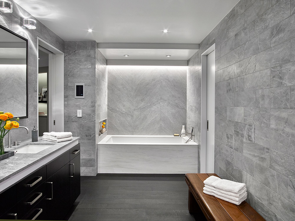 На фото: главная ванная комната в стиле модернизм с плоскими фасадами, темными деревянными фасадами, полновстраиваемой ванной, душем в нише, инсталляцией, серой плиткой, каменной плиткой, серыми стенами, темным паркетным полом, врезной раковиной и мраморной столешницей с