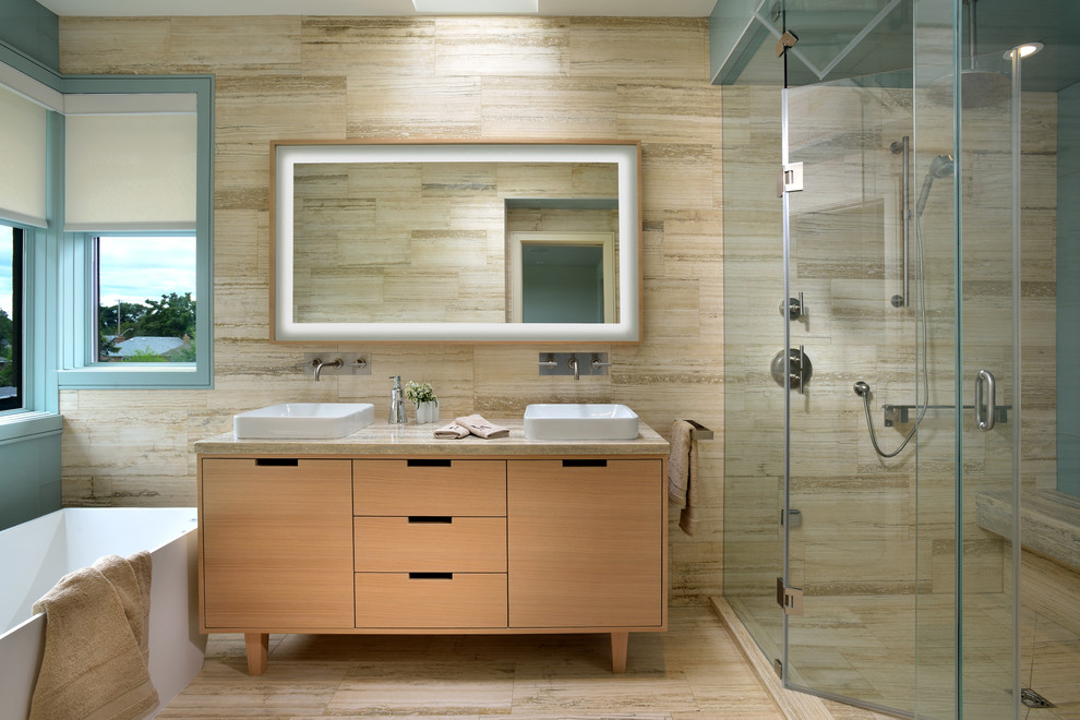 Inredning av ett nordiskt mellanstort en-suite badrum, med ett fristående handfat, släta luckor, skåp i ljust trä, bänkskiva i kalksten, ett fristående badkar, en dubbeldusch, en vägghängd toalettstol, flerfärgad kakel, stenkakel och kalkstensgolv